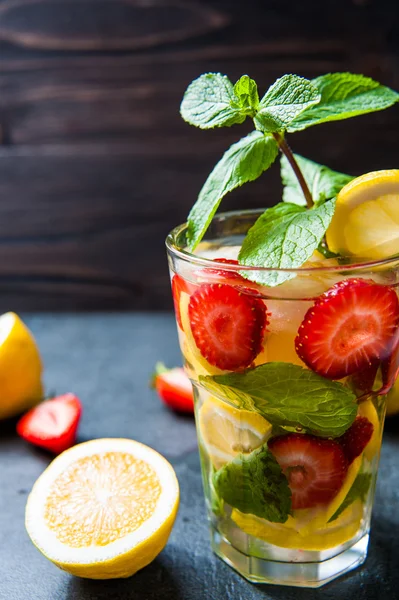 Strawberry lemonade and ingredients - strawberry, lemon, dark stone background.