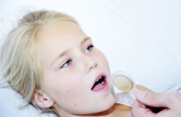 Sick girl taking medicine from a spoon laying in bed