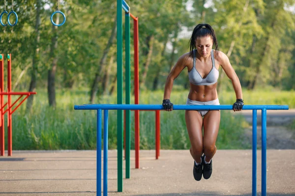 Beautiful fitness woman doing exercise on parallel bars sunny outdoor. Sporty girl doing push ups on bars outdoor