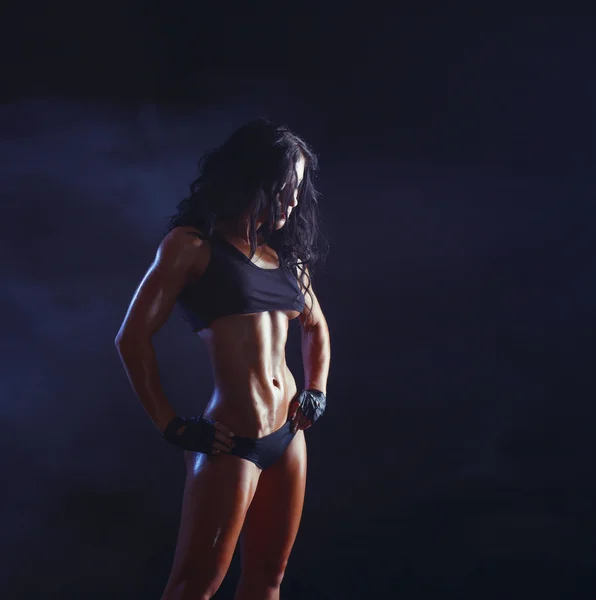 Sexy young muscled fitness brunette girl posing over black background. Fitness woman in sport wear with perfect fitness body