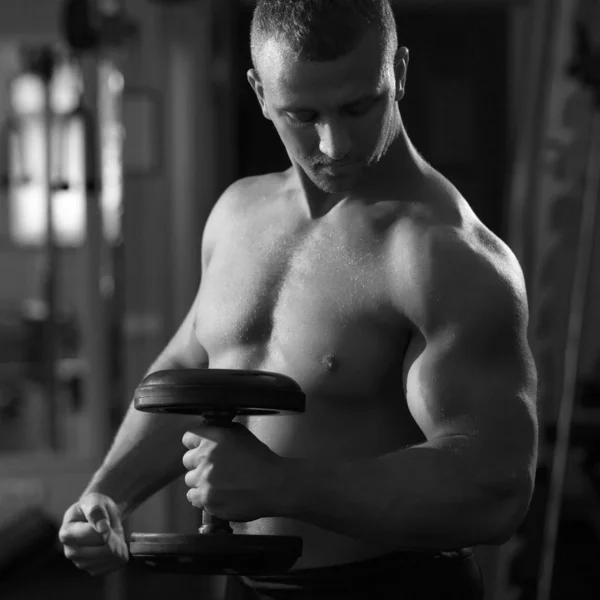 Muscular man working out with dumbbells looking to his biceps