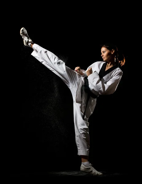 Young woman giving a kick on black background