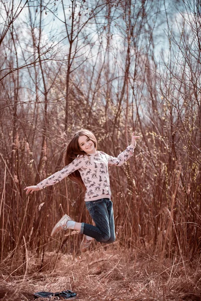 Smiling kid girl jumping on grass in meadow. Looking at camera. Childhood. Back to school.
