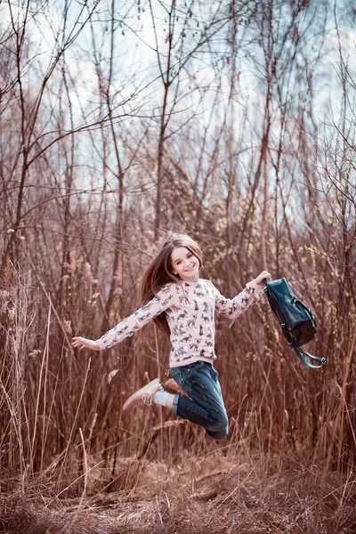 Smiling kid girl jumping on grass in meadow. Looking at camera. Childhood. Back to school.