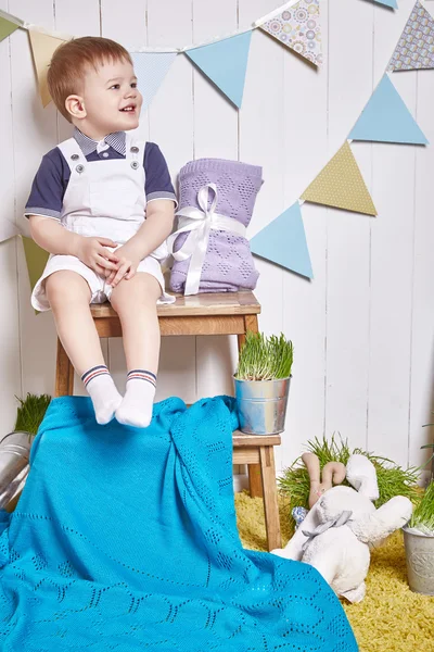 Beautiful little baby boy sitting on a chair with a knitted blanket Easter basket with colored eggs hay, Easter Bunny, a holy religious holiday, a happy guy cute child funny kid