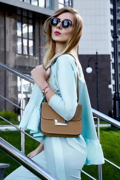 Fashion beautiful sexy woman blonde hair wear stylish trend clothes costume organic materials sunglasses luxury life style brand accessory lather bag outdoor of modern building summer time model