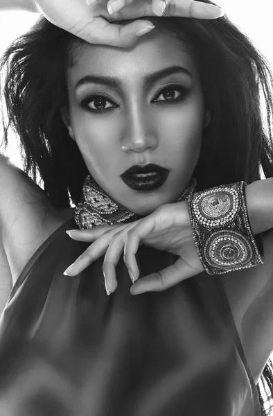 Black and white fashion portrait of the beautiful mulatto with dark skin, hair and red lips in traditional ethnic accessories, and bracelet on her hand