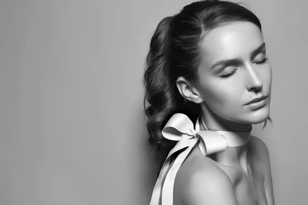 Black and white tender profile fashion portrait of Beautiful gentle young brunette woman with close soft eyes and sensitive mouth wearing silk bow on the neck and right shoulder