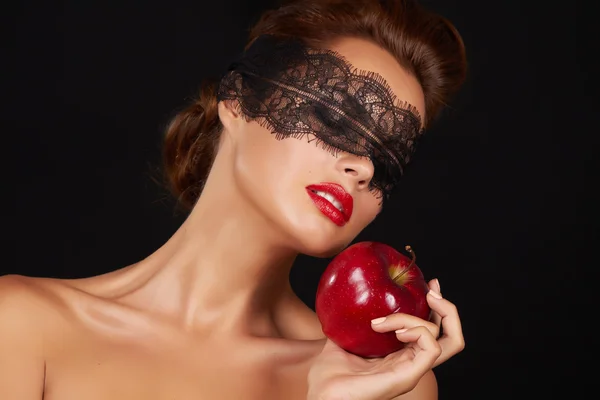 Young beautiful sexy woman with dark lace on eyes bare shoulders and neck, holding big red apple to enjoy the taste and are dieting, feeling temptation, teeth passion sex red lips
