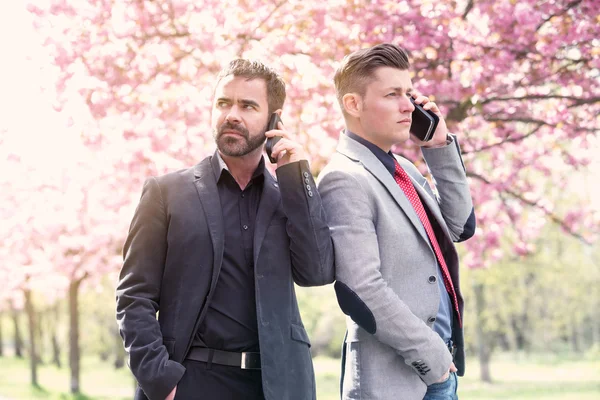 Two businessmen outside talking on the phone