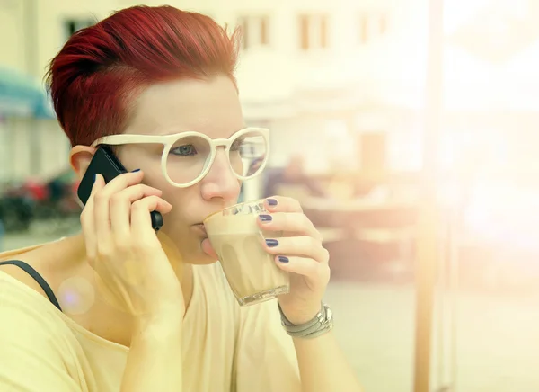 Red-haired woman drinking coffee and talking on the phone