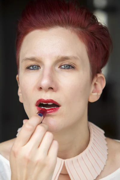 Redhaired woman putting red lipstick on