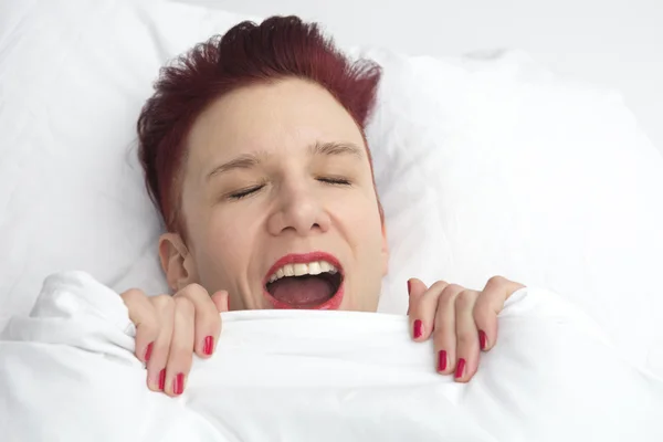 Red-haired woman yawning in bed