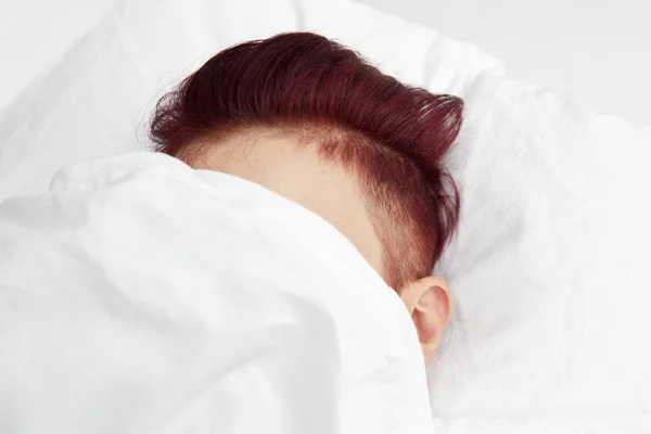 Red-haired head in bed covered by bedsheets