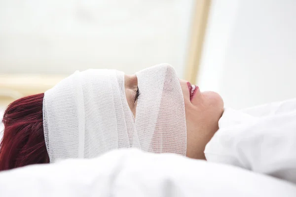 Closeup of woman in bed with bandages wrapped around her head