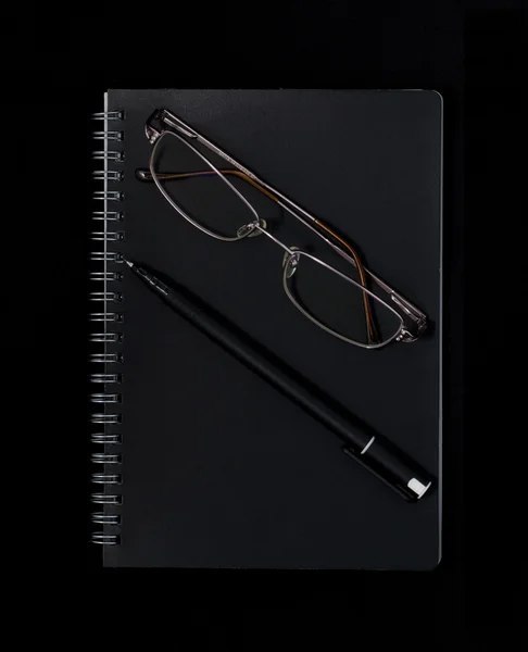 Notebook, pen and glasses on a dark background
