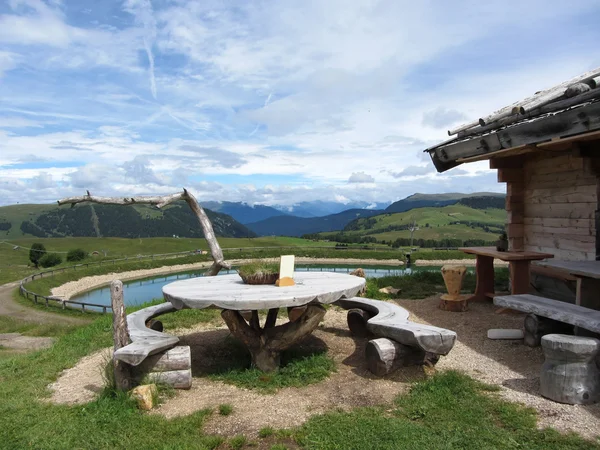 Wooden table next to hut cabin in mountain alps . Panoramic mountain view of the Dolomites in background . Alpe di Siusi, South Tyrol - Italy