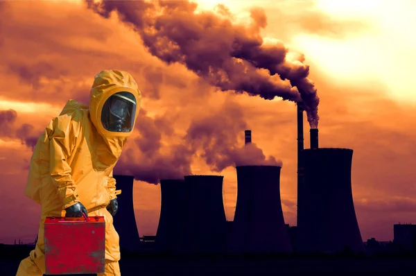 View of smoking coal power plant at sunset and men in protective hazmat suit