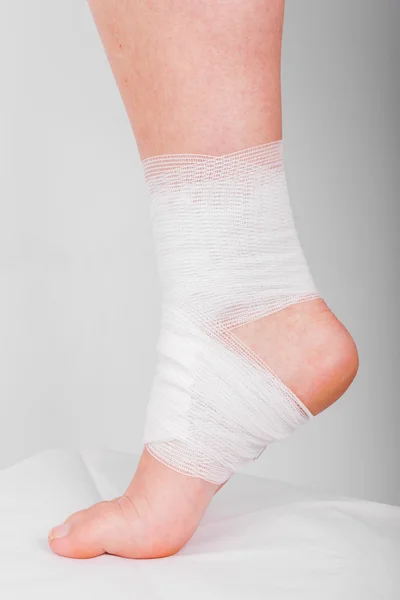 Injured ankle with bandage on a grey background