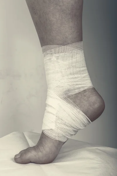 Injured ankle with bandage on a grey background