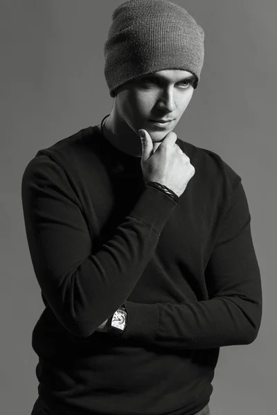 Portrait of trendy guy wearing  black jumpers and grey  hat, arms on his pocket in jeans. the concept of a gangster guy