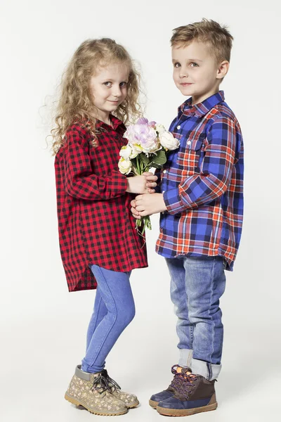 Funny lovely children.  fashionable little boy and girl in  jeans and plaid shirts. little boy gives flowers to girl. stylish kids in casual shoes. fashion children