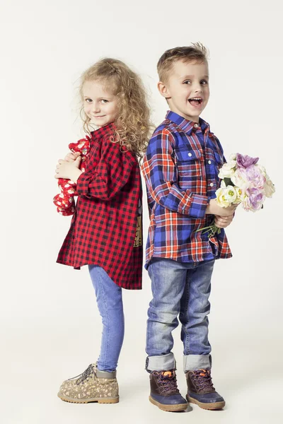 Funny lovely children.  fashionable little boy and girl in  jeans and plaid shirts. little boy gives flowers to girl. stylish kids in casual shoes. fashion children