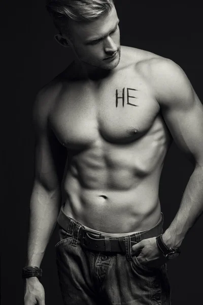 Handsome muscular male model with intense glance posing over grey background. Perfect body with the inscription \