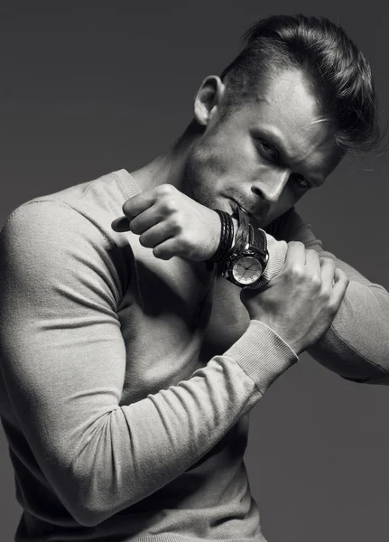 Advertising wrist watch concept. Beautiful (handsome) muscular male model with perfect body in grey jumper. He bites and unfastens the bracelet from the clock. Street style. Black and white, monochrome studio shot