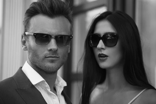 Young Happy fashionable couple in the city in stylish sunglasses.The man Wearing in business suit, the woman in romantic sexy dress with lace and coat
