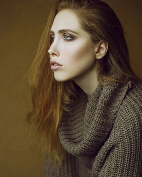 Studio shot. Emotive portrait of fashionable model with long curly red hair and natural make-up posing over wooden background. Perfect skin and green eyes. Urban style.