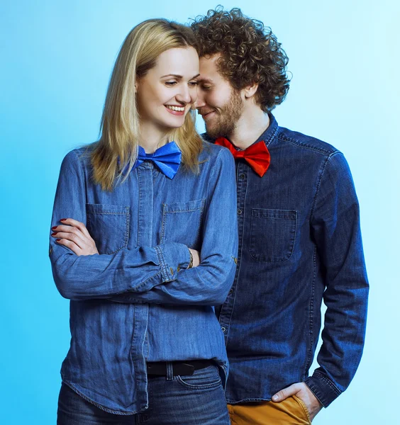 Portrait of gorgeous blond fashion man and woman in jeans shirt and funny bow tie, posing on blue background. Perfect skin and hairdo. Vogue style. Studio shot. Lifestyle concept