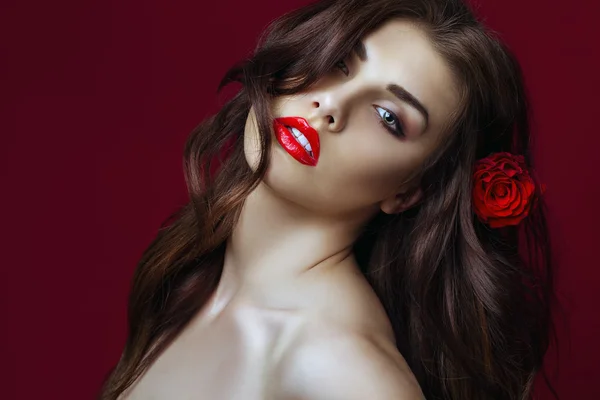 Beautiful Sexy fashion Woman with rose in her hair.  Makeup with  Red Lips, long perfect hair and Red rose. Beauty italian Girl. Passion. Close up. Copy space