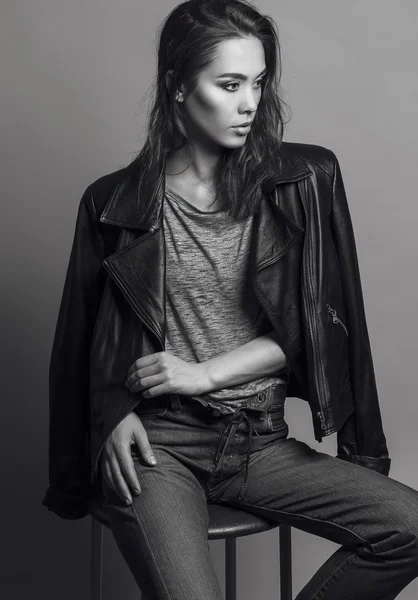 Portrait of a fashionable model with natural make up and perfect skin, dressed in men's jeans, grey shirt, black jacket and sneakers.  Studio shot. High fashion look. Monochrome (black and white)  photo