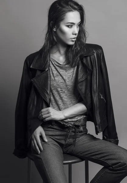 Portrait of a fashionable model with natural make up and perfect skin, dressed in men\'s jeans, grey shirt, black jacket and sneakers.  Studio shot. High fashion look. Monochrome (black and white)  photo