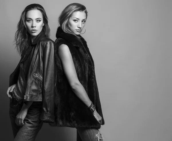 Fashion shot of two elegant beautiful girls (brunette and blonde) in studio on grey background, dressed in casual clothes . Shopping inspiration. Monochrome (black and white)  photo