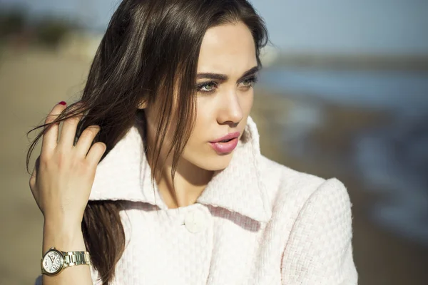 High fashion concept. Emotive portrait of beautiful brunette with long  hair and perfect make up, wearing in pink coat. the sunny weather on  beach. Italian luxurious style. Outdoor shot