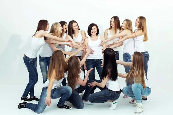 Happy together concept. Group portrait of healthy girls in white t-shirts and blue jeans sitting and posing over white background. Copy-space. Urban style. Studio shot