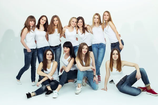 Happy together concept. Group portrait of healthy girls in white t-shirts and blue jeans sitting and posing over white background. Copy-space. Urban style. Studio shot