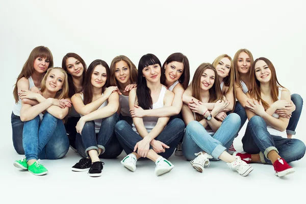 Happy together concept. Group portrait of healthy girls in white t-shirts and blue jeans sitting and posing over white background. Copy-space. Urban style. Studio shot