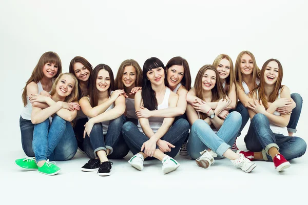 Happy together concept. Group portrait of healthy girls in white t-shirts and blue jeans sitting and posing over white background. Copy-space. Urban style. Studio shot