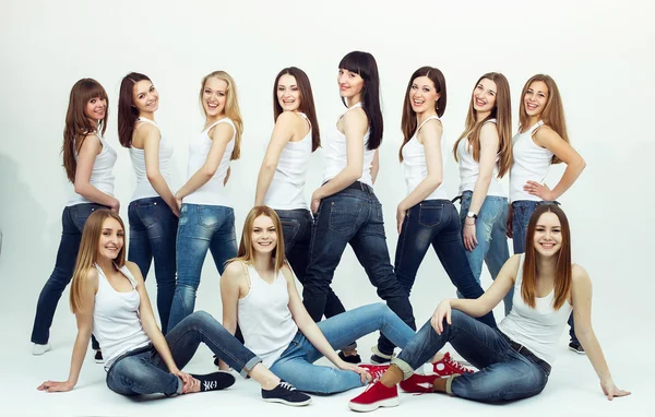 Happy together concept. Group portrait of healthy girls in white t-shirts and blue jeans sitting and posing over white background. Copy-space. Urban style. Studio shot