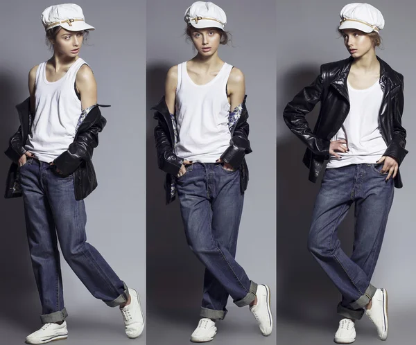 High fashion look. Portrait of a fashionable model with natural make up and perfect skin, dressed in men\'s jeans, white shirt, black jacket, stylish white hat and sneakers.  Studio shot