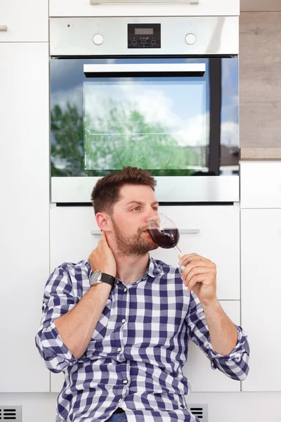 Attractive young man with a glass of wine in a modern kitchen.