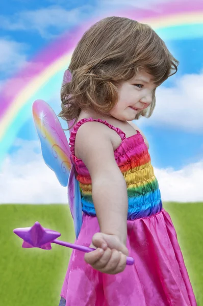Girl with fairy dress and wand standing under a colorful rainbow