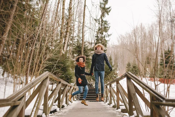 Young happy couple holding hands and jumping in winter park