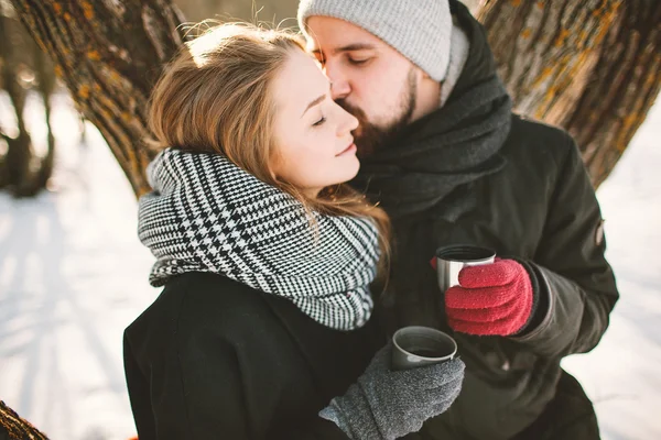 Hipster couple in winter park with hot tea from thermos