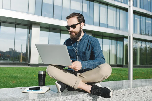 Businessman in sunglasses with laptop outdoors in front of offic