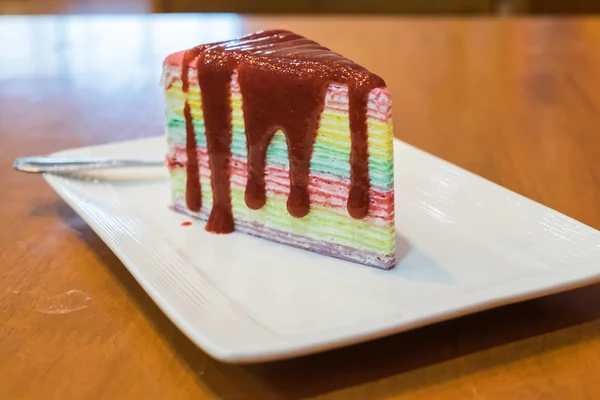 Sliced of rainbow crepe cake with strawberry sauce