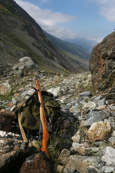 Backpack and rifle hunter on the rocks at the entrance to the rise in the valley, the Northern Caucasus,